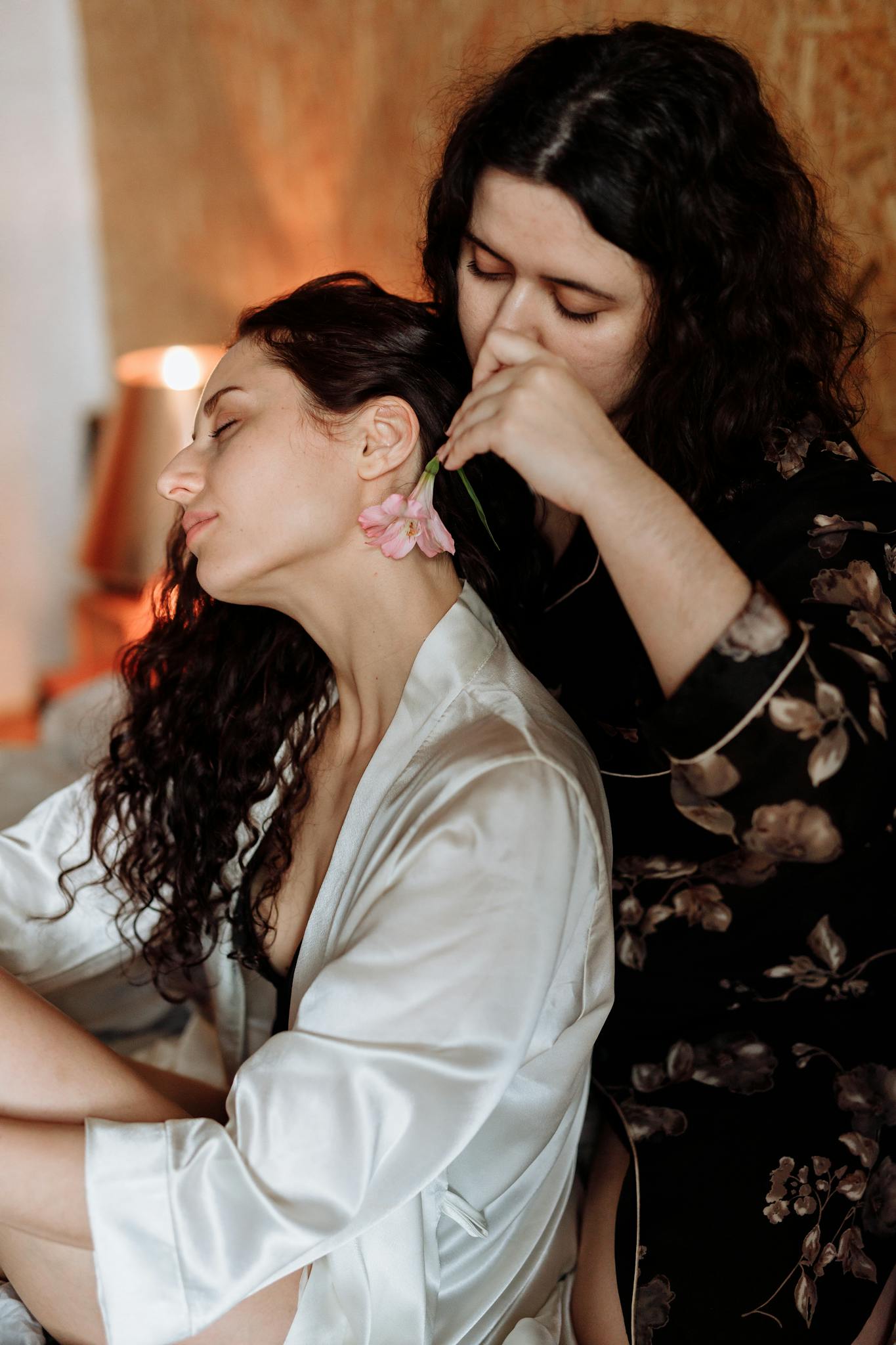 A heartfelt moment between two women, one placing a flower behind the other's ear.